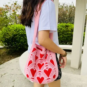 Primer plano detallado del bolso de punto rosa con patrones de corazones rojos y diseño ajurado.
