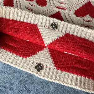 Vista detallada de la textura del bolso de punto rojo y blanco con botones de presión metálicos.