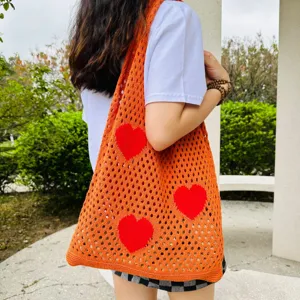 Nahaufnahme der stylischen orangefarbenen Häkel-Tasche mit rotem Herz-Muster und Lochstrick-Detail.