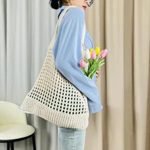 Detailaufnahme einer beige gestrickten Schulter-Tragetasche am Modell im gemütlichen Raum.
