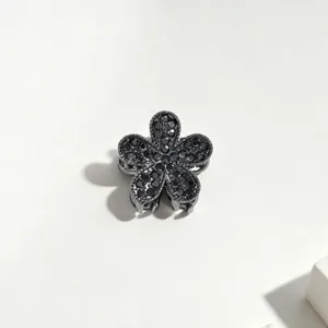 Primo piano dettagliato di un mini fermaglio per capelli a fiore in metallo con strass scuri.