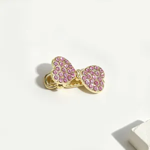 Dettaglio in primo piano di una mini molletta dorata con strass rosa scintillanti.