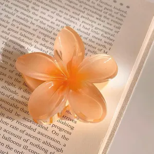 Close-up detail of a translucent jelly orange plumeria flower hair claw clip on book background.