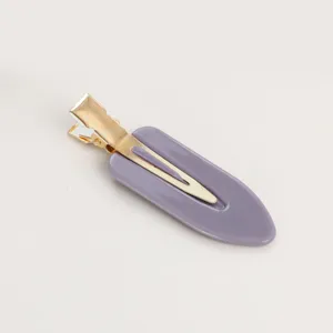 Dettaglio in primo piano della molletta per capelli a goccia viola con clip dorata.