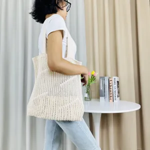 Detail view of a beige knitted hollow shoulder tote bag styled in a bright indoor room.