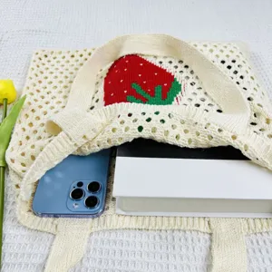 Nahaufnahme einer niedlichen gestrickten Erdbeere-Tragetasche mit Netzdesign und Requisiten.