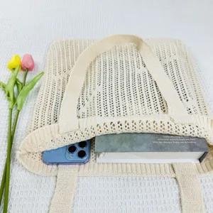 Detailed close-up view of the beige knitted hollow-out shoulder tote bag with a book.