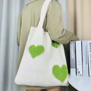 Detailansicht der beige Strick-Tragetasche mit grünen Plüschherzen und Perlendetails.