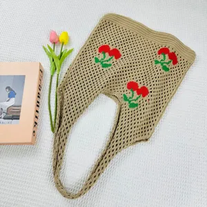 Primer plano de un elegante bolso tote de ganchillo beige con bonito diseño de cerezas rojas.