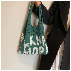 Gruene gestrickte Tasche mit weissen Buchstaben, laessige Schultertasche im Alltag.
