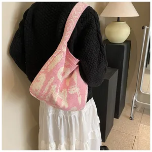 Detailansicht einer stilvollen rosa-weißen Strick-Umhängetasche, getragen im schicken Zimmer.