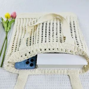 Detailaufnahme einer beige geflochtenen Strick-Tragetasche mit Telefon und Buch.