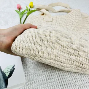 Primo piano sulla texture della borsa shopper in maglia beige, con tessuto morbido e manici.