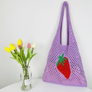 Detailaufnahme einer lila gestrickten Netztasche mit eingewebtem roten Erdbeermuster.