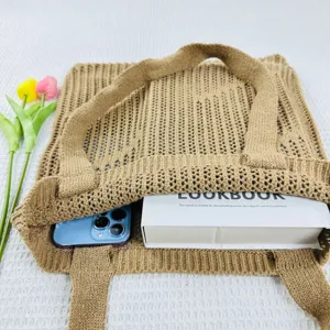 Detailed view of the stylish khaki hollow knitted tote bag styled with a phone and book.