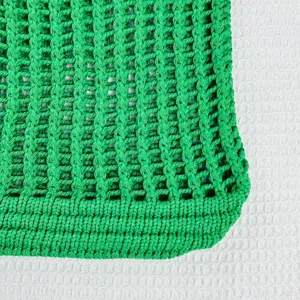 Gros plan sur la texture du sac de plage ajouré en tricot vert, montrant un maillage solide.