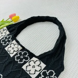 Close-up of black and white knit tote bag featuring floral pattern and cable knit texture details.