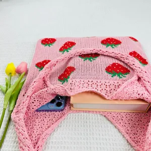 Roze gebreide aardbei tote tas detail toont de binnenste opslagcapaciteit met boek en telefoon.