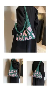 Detailansicht der grünen Strick-Tasche mit rosa Buchstaben, getragen auf Schulter, stylisch.