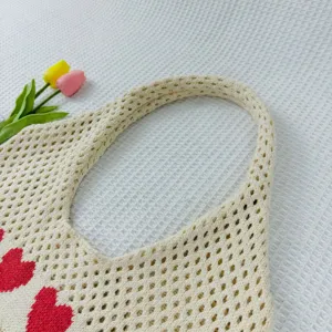 Beige Strick-Netz-Tragetasche Detail zeigt rotes Herzmuster und weiche Textur nahaufnahme.