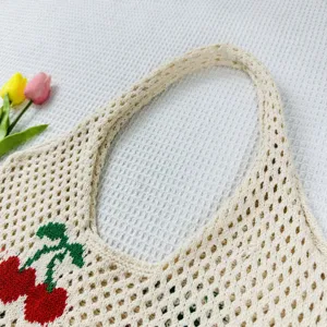 Primer plano detallado del bolso de mano de ganchillo beige con motivo de cerezas rojas.