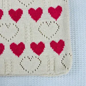 Stricktasche Detail mit rotem Herzmuster und Zopfmuster auf altweißem Textilgewebe.