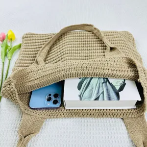 Dettaglio della borsa shopper in maglia beige con telefono e libro all'interno