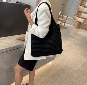 Borsa shopper in maglia nera indossata a spalla, dettaglio di grande borsa casual lavorata a maglia.