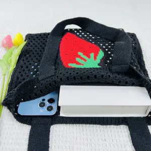 Detailansicht einer schwarzen Stricktasche mit rotem Erdbeermuster und praktischen Henkeln.