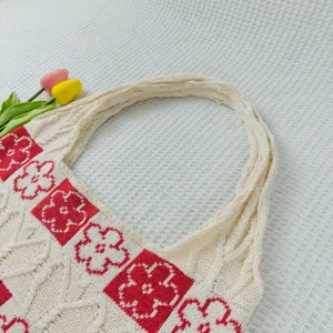 Knitted tote bag detail shot showing white cable knit texture and red floral square pattern.
