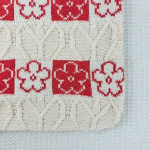 Detailed knit tote bag featuring a charming red and white floral pattern and classic cable knit.