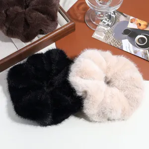 Close-up of fluffy faux fur hair scrunchies in black, beige, and brown on a styled tabletop.