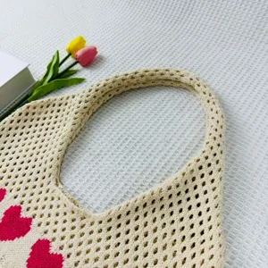 Detailaufnahme der beigen Stricktasche mit rosafarbenem Herzmuster und Strukturhintergrund.