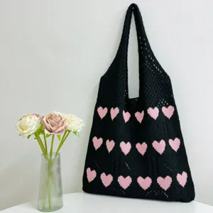 Nahaufnahme der schwarzen Stricktasche mit rosafarbenem Herzmuster und feiner Textur.