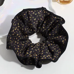 Close-up detail of a large black and gold leopard print hair scrunchie with neat stitched edges.