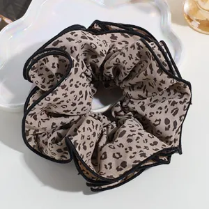 Oversized leopard print hair scrunchie with black trim, stylish hair tie detail shot.