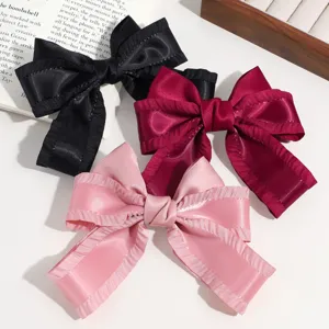 Detalle de pinzas para el cabello con lazos de saten en negro, burdeos y rosa con bordes rizados.