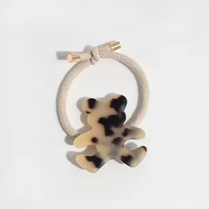 Detailed close-up of a chic tortoiseshell resin bear hair tie with golden metallic ends.