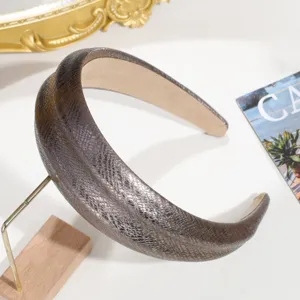 Vista detallada de diadema ancha de cuero con textura de serpiente y brillo metálico en soporte.