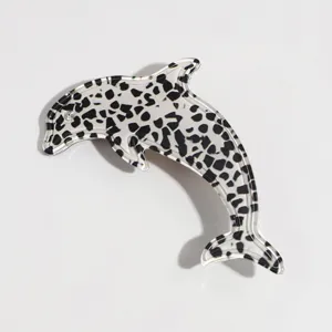 Primer plano de una pinza de pelo en acrilico con forma de delfin y patron negro y blanco.