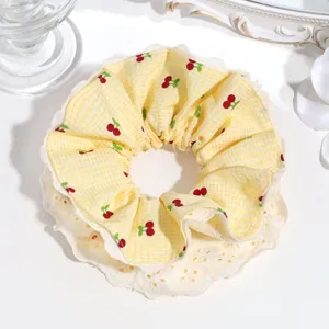 Closeup detail of yellow gingham cherry print hair scrunchie with white lace layer trim.