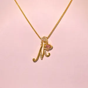 Gold letter necklace detail with sparkling rhinestones and pink heart orb pendant.