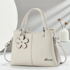 Elegante borsa in pelle beige con ciondolo floreale, doppi manici e tracolla elegante.