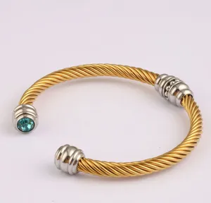 Gros plan du bracelet jonc câble doré avec embouts argentés et pierre bleue élégante.