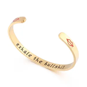 Bracelet manchette en acier inoxydable doré avec citation gravée et lèvres rouges.