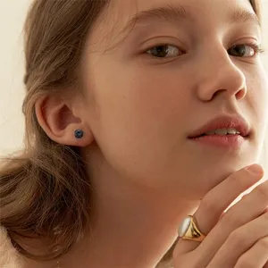Close-up detail shot of minimalist black stud earrings and gold ring worn by a female model.