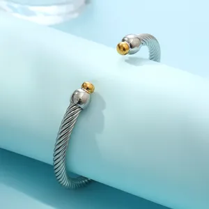 Bracelet manchette torsadé en acier inoxydable avec finition bicolore et embouts boules dorés.