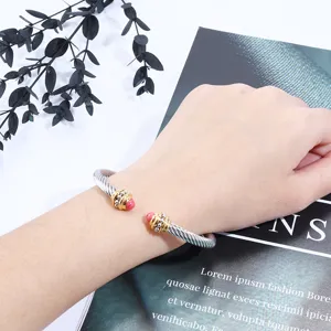 Bracelet manchette torsadé tendance pour femme avec embouts dorés et perles roses.