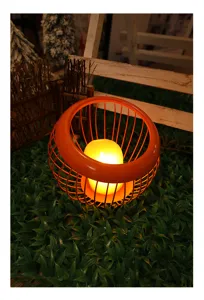 Cesto di frutta in filo metallico arancione con candela LED in dettaglio di giardino.