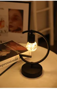 Detail van de minimalistische G-vormige tafellamp met warme lichtlingers aan de binnenkant.